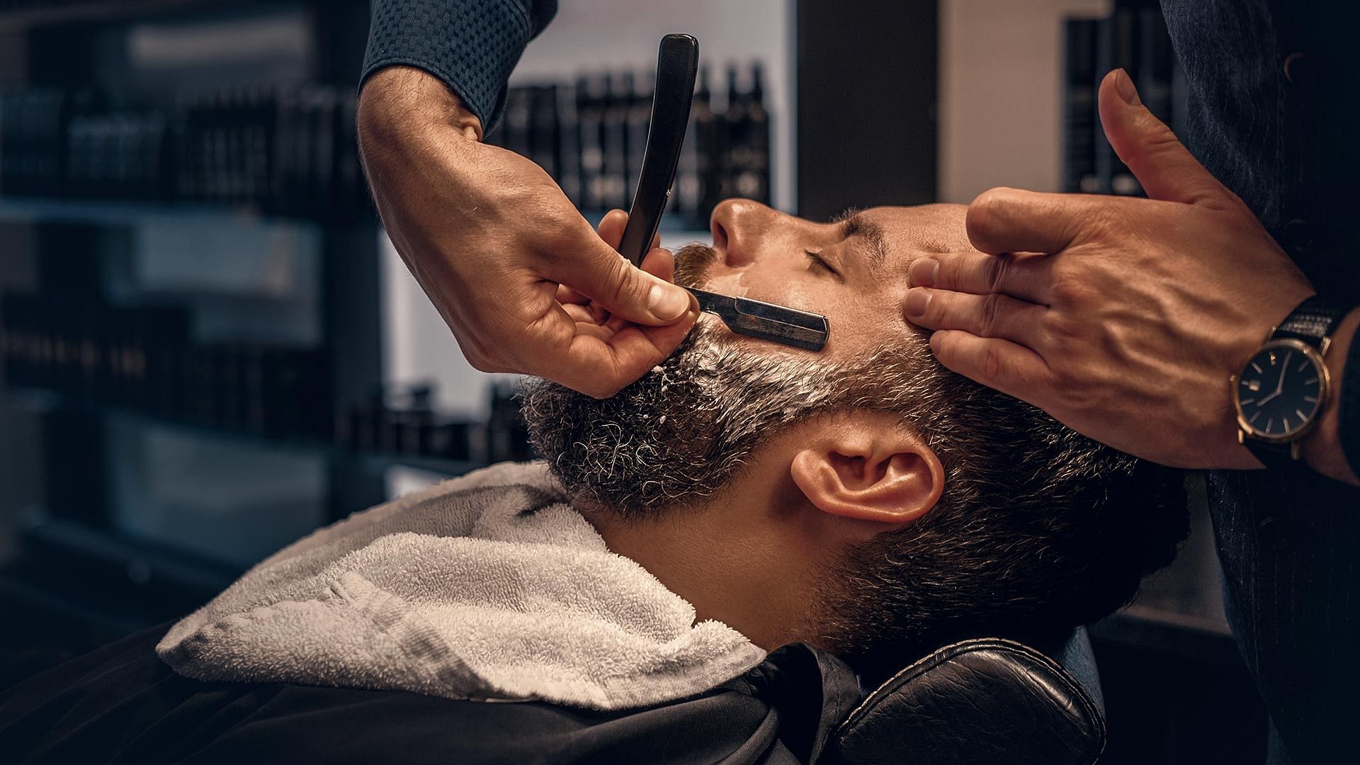 Barber shaping a man's beard with a straight razor.
